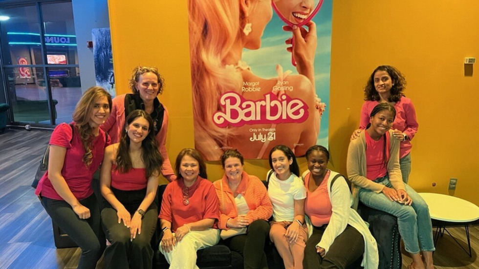 several people posing in front of a poster for the Barbie movie