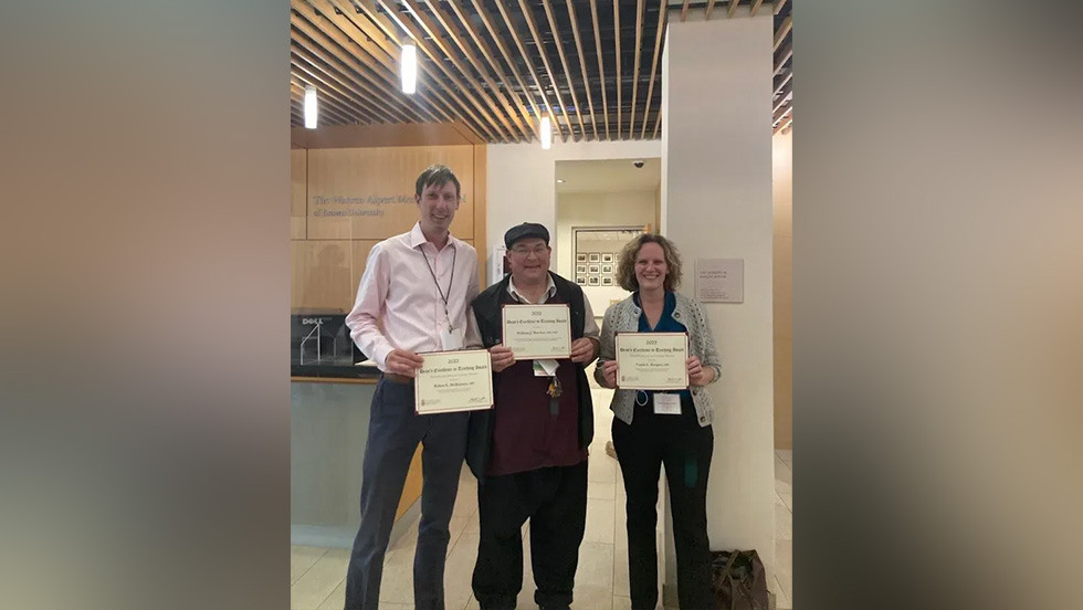 three people posing together and holding pieces of paper